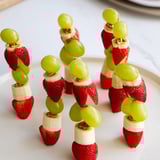 Nahaufnahme von bunten Elf-Hut Erdbeer-Spießen, garniert mit cremiger Sahne, bereit zum Servieren.