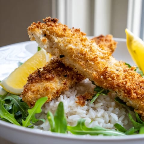 Crispy Parmesan Chicken Cutlet Bowl mit knusprigen panierten Schnitzeln auf fluffigem Reis und frischer Rucola, verfeinert mit Zitrone.