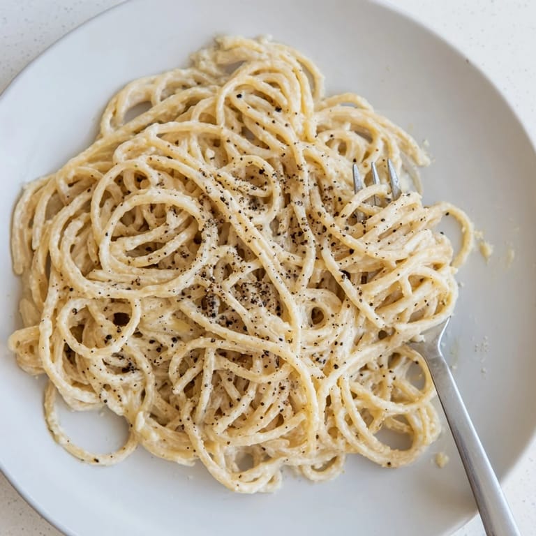 Ein Teller Spaghetti Cacio e Pepe, umrandet von würziger schwarzer Pfefferfrucht.